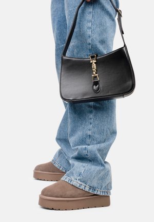 Sac en cuir noir au design structuré, avec des accessoires en or et une courte poignée, associé à un denim bleu clair et des chaussures à plateforme marron.