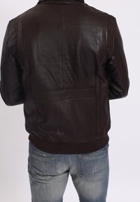 Hnědá kožená bunda s hladkou texturou, žebrovaným lemem a ramenními epolety. Nositelná přes modré džíny.