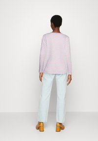 Camisa de manga longa com riscas horizontais em rosa e branco, combinada com calças largas de ganga clara e sapatos de salto bloco em tom bege.