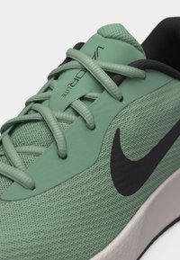 Κοντινό πλάνο πράσινου αθλητικού παπουτσιού τρεξίματος Nike με μαύρο λογότυπο Swoosh, ύφασμα από δίχτυ και διασταυρούμενα κορδόνια πάνω στη γλώσσα με την ετικέτα "VaporLite".