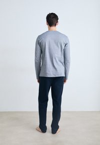 Camisa gris de manga larga combinada con pantalones navy. La camisa presenta un cuello redondo y una textura mínima, mientras que los pantalones tienen un corte recto.