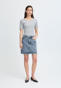 Un haut gris à rayures avec des manches courtes associé à une jupe en denim bleue dotée d'une taille, de poches et d'une silhouette droite, le tout complété par des chaussures noires à bout carré.
