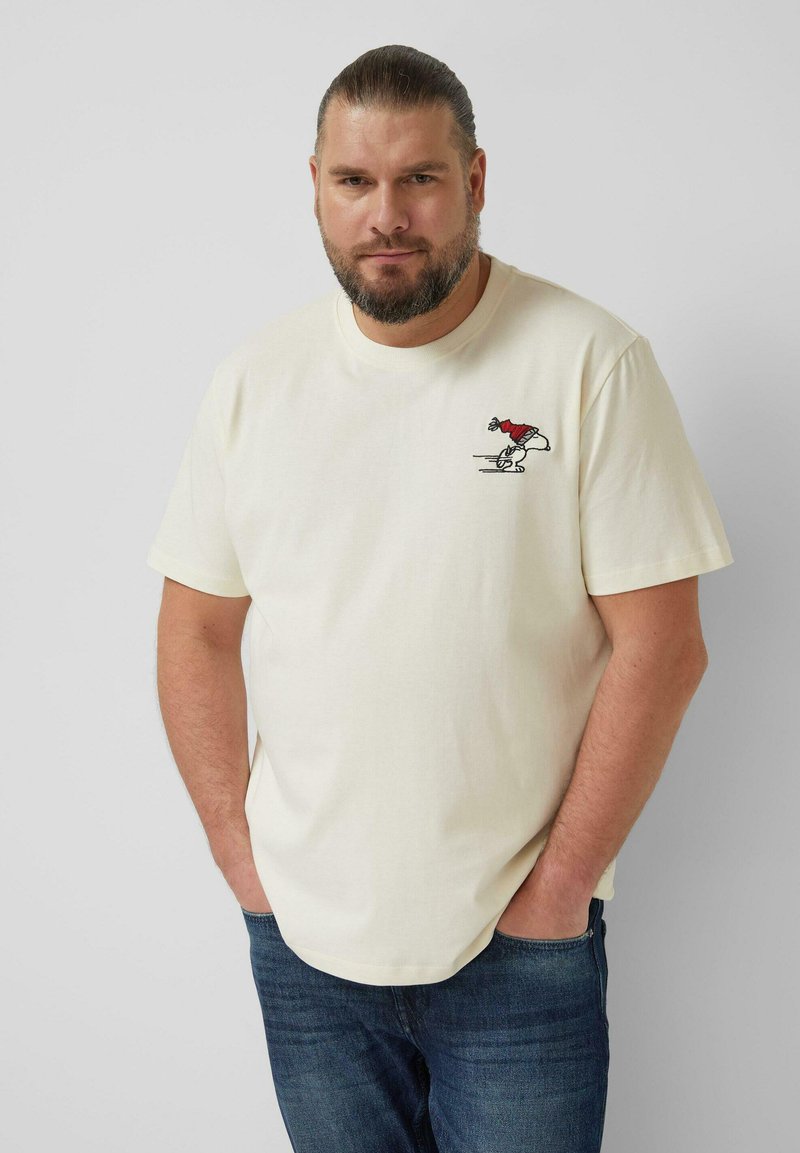 Cremefarbenes Baumwoll-T-Shirt mit einer kleinen, gestickten Cartoon-Figur in rotem Hemd. Klassische Passform mit kurzen Ärmeln und rundem Halsausschnitt.