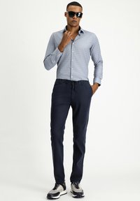 Camicia azzurra chiara a righe con pois bianchi, abbinata a pantaloni blu navy e sneakers nere, accessoriata con occhiali da sole neri.