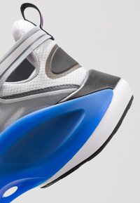 Grauer und weißer Sneaker mit Obermaterial aus Mesh, blauer Sohle und schwarzen Akzenten. Verfügt über ein geschwungenes Design und markante Überlagerungsdetails.