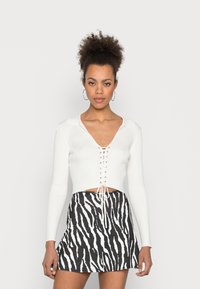 Top cropped branco canelado com um decote em V profundo e detalhe de atacadores na parte da frente, combinado com uma saia mini com estampa de zebra em preto e branco.