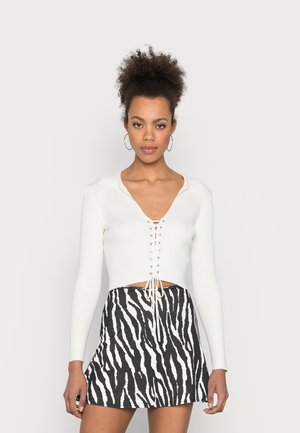 Top cropped branco canelado com um decote em V profundo e detalhe de atacadores na parte da frente, combinado com uma saia mini com estampa de zebra em preto e branco.
