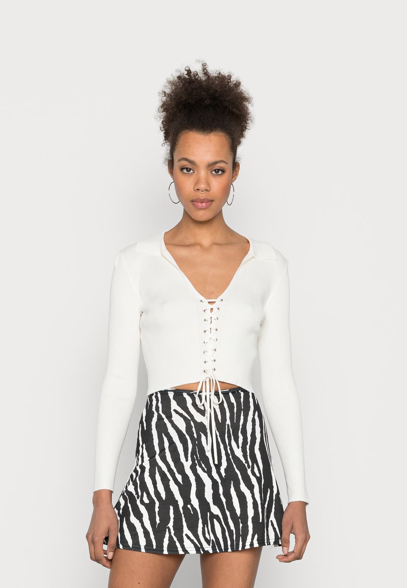 Top cropped branco canelado com um decote em V profundo e detalhe de atacadores na parte da frente, combinado com uma saia mini com estampa de zebra em preto e branco.