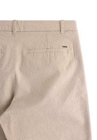 Béžové kalhoty s hladkým textilním povrchem, s jednou kapsou na zadní straně a malým kovovým logem blízko pásku. Jednoduchý design.