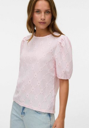 Pink puff-sleeve blouse with embroidered diamond patterns and eyelet details, made of textured fabric. Styled with light blue jeans.