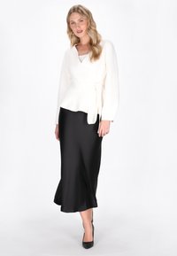 Biała bluzka w stylu owinięcia z długimi rękawami, połączona z elegancką czarną satynową spódnicą. Ubranie ma akcent w postaci zawiązanego pasa.