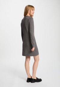 Graues Langarmkleid aus weichem Stoff, mit rundem Ausschnitt und lässiger Passform, kombiniert mit schwarzen, glanzenden Schuhen.