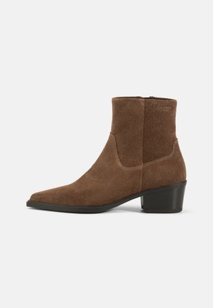Brune suède ankel støvlett med spiss tå og lav blokkhæl. Har minimal søm og glidelås lukking bak.