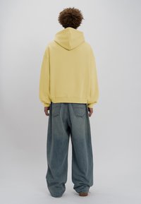 Felpa gialla con cappuccio dal fit rilassato, abbinata a jeans in denim chiaro a vestibilità ampia, con un semplice design della tasca posteriore.