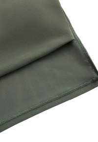 Gros plan d'un tissu vert olive plié montrant des textures lisses et en maille avec des bords cousus sur un fond blanc.