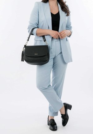 Mustalla nahkakäsilaukku tekstuuripinnalla, hopeaosilla ja tupsukoristeella, yhdistettynä vaaleansiniseen muotipukuun ja mustiin kenkiin.