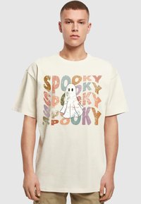Krémové bavlněné tričko s grafikou ducha a barevným, opotřebovaným textem, který říká "SPOOKY" v oranžové, fialové a zelené barvě.