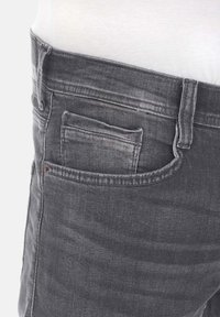 Jeans de mezclilla gris con un acabado desgastado, que cuentan con un bolsillo delantero, lazos para el cinturón y una superficie texturizada. Vista en primer plano del área de la cinturilla.