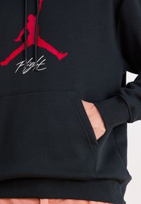 Sudadera negra con logo rojo de Jumpman y texto "Flight". Fabricada con una tela suave, cuenta con un bolsillo frontal y una capucha ajustable con cordones.