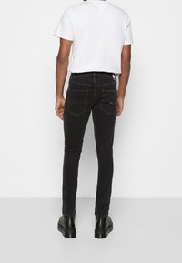 Svarta denim skinny jeans med två bakfickor och en logotagg på midjan, tillsammans med en slät vit t-shirt och svarta skor.