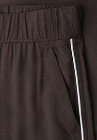 Pantalon marron foncé avec taille élastique et détail de passepoil blanc vertical le long de la couture latérale près de l’ouverture de la poche.