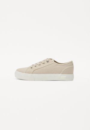 Beżowe sneakersy z płótna z zaokrąglonym noskiem, sznurowanym zapięciem i gumową podeszwą. Charakteryzują się delikatnym przeszyciem oraz markową metką po boku.