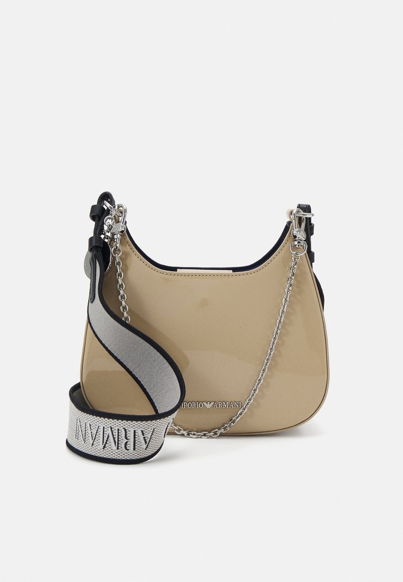 Beige patenttinahkainen käsilaukku, jossa on pyöreä muoto, hopeinen ketjuyksityiskohta ja harmaa hihna, jossa on logoteksti. Reunoissa mustaa kontrastia.