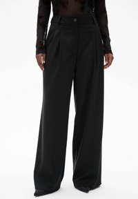 Zwarte wijde broek met een sleek, gladde textuur en voorplooien. Heeft een enkele knoopsluiting bij de taille en een hoge taille pasvorm.