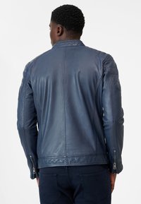 Marineblaue Lederjacke mit figurbetontem Design, gesteppten Schulterakzenten und Reißverschlussdetails an den Ärmeln. Glatte Textur und klassischer Schnitt.