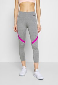 Grå cropped leggings med en glat overflade, der har en pink accentstribe og Nike-branding. Parret med hvide sportsko.