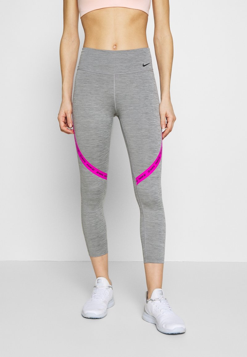 Grå cropped leggings med en glat overflade, der har en pink accentstribe og Nike-branding. Parret med hvide sportsko.