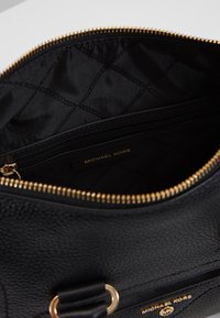 Borsa in pelle nera con zip dorata aperta per rivelare un rivestimento interno trapuntato e una tasca con zip etichettata Michael Kors.