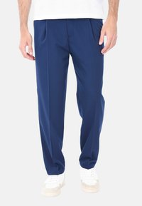 Pantaloni blu navy con un taglio dritto, pieghe frontali e un tessuto liscio e leggero. Abbinati a sneakers bianche per contrasto.