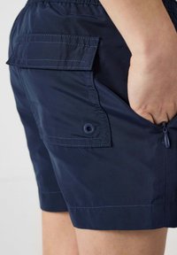 Pantaloni corti blu navy realizzati in tessuto leggero, dotati di una tasca a patta sul retro, cintura elastica e dettagli di tasca con zip.