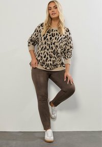Beige stickad tröja med leopardsmönster, långa ärmar och rundad hals. Matchad med bruna tighta byxor och vita sneakers med bruna sulor.