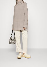 Beige knit turtleneck sweater with long sleeves, cream trousers, and light wooden-soled clogs. Zebra print handbag with a black strap.