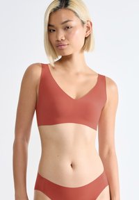 V-hals bralette in een gedempte terracotta kleur, gemaakt van zachte stof met brede schouderbanden en een naadloos ontwerp. Minimalistische stijl.
