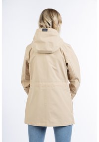 Chaqueta impermeable beige con capucha, textura suave y bolsillos laterales; cuenta con un parche con el logo en la parte posterior cerca del cuello.