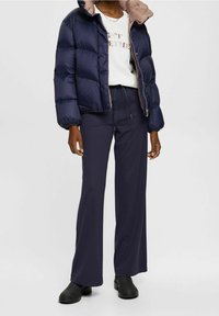 Chaqueta de plumas navy con interior beige, combinada con una camiseta gráfica blanca y pantalones oscuros de pierna ancha; unas botas negras de tobillo completan el look.