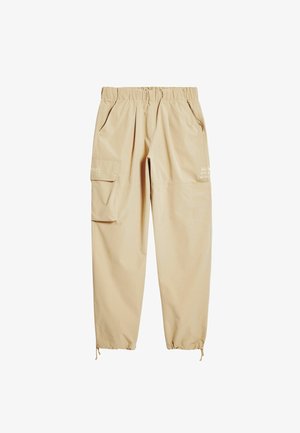 Béžové cargo kalhoty vyrobené z lehkého materiálu, s elastickým páskem, bočními kapsami a šňůrkou na kotníku. Obsahují potištěný text.