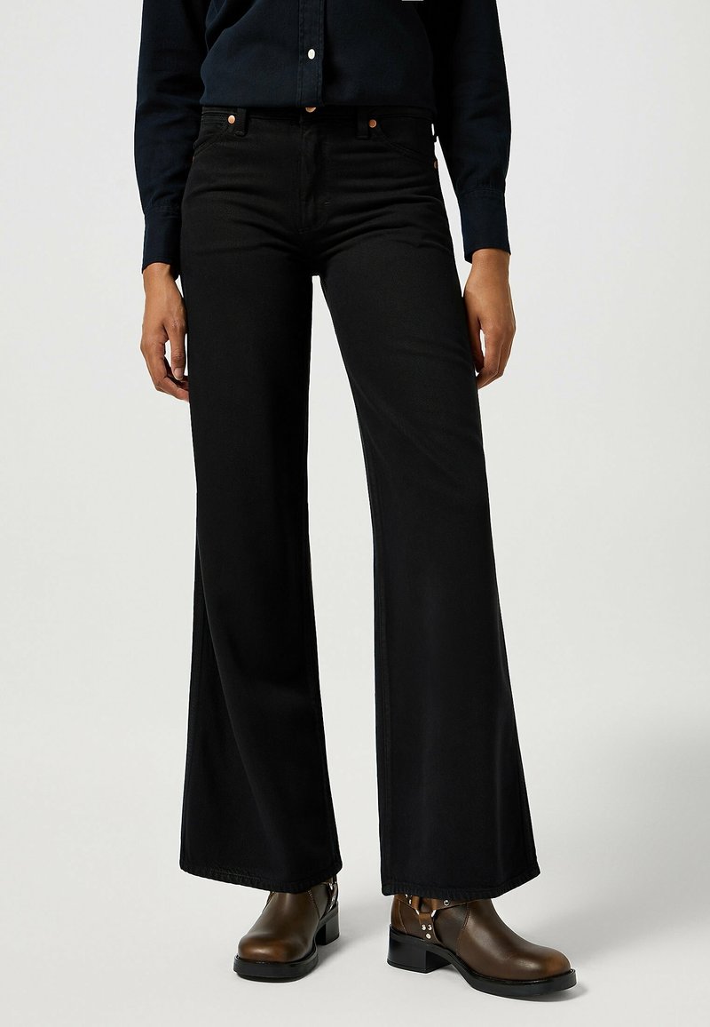 Black wide-leg jeans made from denim with a smooth texture, featuring orange stitching and button details, paired with brown ankle boots.