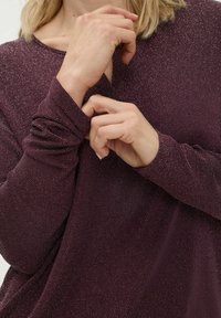 Bordeauxrode top met lange mouwen en een relaxed model, met subtiele metallic spikkels en een verlengd manchetdetail bij de pols.