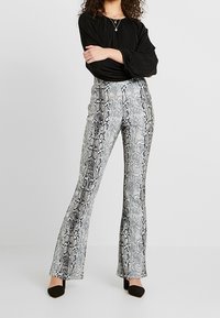 Spodnie dzwony w czarno-białym wzorze wężowym, charakteryzujące się gładką fakturą i dopasowanym krojem, w połączeniu z czarną bluzką.