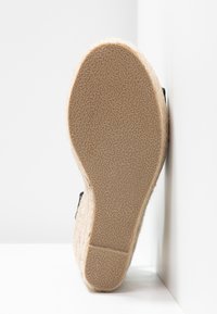 Semelle d'espadrille avec une finition en jute naturel texturé, tige en toile noire et un léger talon surélevé.
