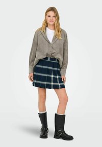 Pelēka zamša oversized jaciņa, balta T-krekls, tumši zila tartāna seles svārki un melni ādas zābaki līdz ceļgaliem ar sprādzēm un akcentiem.