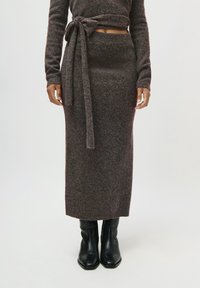 Ensemble en maille composé de deux pièces comprenant une jupe ajustée à motifs marron et gris, un haut à manches longues assorti et un détail de taille nouée. Bottines noires à la cheville.