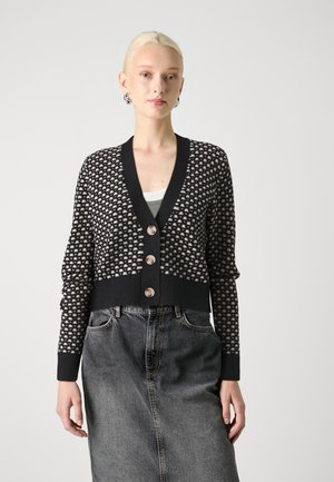 Melnā un krēmkrāsā rakstota kardigāna ar dziļu V-veida kakla izgriezumu, ar četriem pogām, ribotām piedurknēm un īsu dizainu, savienots ar džinsu svārkiem.