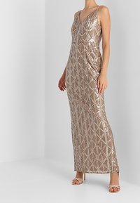 Abito senza maniche in paillettes rose gold con motivo geometrico, scollatura a V e orlo lungo abbinato a sandali con tacco alto e cinturini.