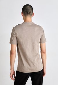Tricou bej cu mânecă scurtă, realizat dintr-un material texturat, având un guler rotund și un design ajustat. Partea din spate are un finisaj neted.
