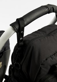 Borsa per pannolini nera fissata con bottoni a pressione e clip al manico di un passeggino bianco avvolto da una presa nera testurizzata.